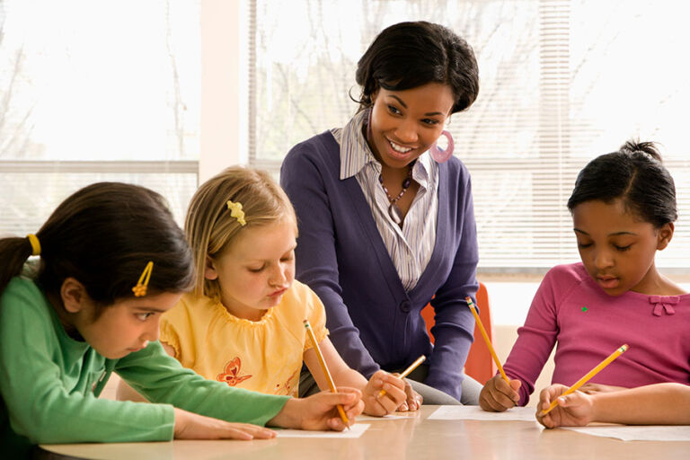 A teacher working closely with young students at their desks